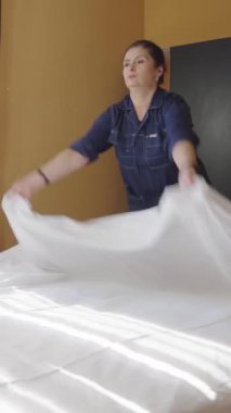 Hizmetçi yatağı kar beyazı bir çarşafla örtüyor. Otel odasında yatak değiştiren bir kadın hizmetçi. Çalışan bir pansiyonda oda temizliyor. Otel işinde kaliteli hizmet