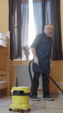 Orta yaşlı bir erkek otel odasını elektrikli süpürgeyle temizliyor. Otel işi konsepti üzerine ticari temizlik şirketi.