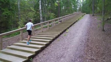 Finlandiya 'da ormandaki doğal bir parkta spor salonunun merdivenlerinde koşan atletik genç bir kadın..