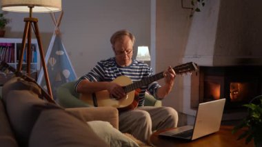 Orta yaşlı bir adam rahat bir odada oturuyor ve akustik gitar çalmayı öğrenmeye odaklanıyor. Önündeki küçük bir masaya yerleştirilmiş dizüstü bilgisayarında bir video dersi izliyor.