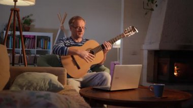 Orta yaşlı bir adam rahat bir odada oturuyor ve akustik gitar çalmayı öğrenmeye odaklanıyor. Önündeki küçük bir masaya yerleştirilmiş dizüstü bilgisayarında bir video dersi izliyor.