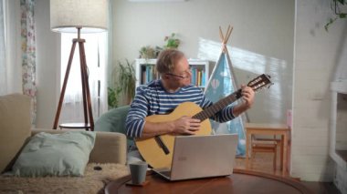 Orta yaşlı bir adam rahat bir odada oturuyor ve akustik gitar çalmayı öğrenmeye odaklanıyor. Önündeki küçük bir masaya yerleştirilmiş dizüstü bilgisayarında bir video dersi izliyor.