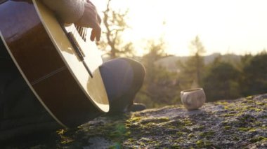 Orta yaşlı bir adam, gün batımında bir Finlandiya ormanında bir uçurumun tepesinde kuksa ahşap fincanlı kahveyle gitar çalar. Sahne, ortamın yumuşak parıltısıyla huzurlu bir çevreyi yakalıyor.