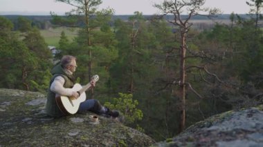 Orta yaşlı bir adam, gün batımında bir Finlandiya ormanında bir uçurumun tepesinde kuksa ahşap fincanlı kahveyle gitar çalar. Sahne, ortamın yumuşak parıltısıyla huzurlu bir çevreyi yakalıyor.