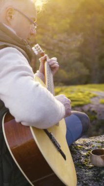 Orta yaşlı bir adam, gün batımında bir Finlandiya ormanında bir uçurumun tepesinde kuksa ahşap fincanlı kahveyle gitar çalar. Sahne, ortamın yumuşak parıltısıyla huzurlu bir çevreyi yakalıyor.