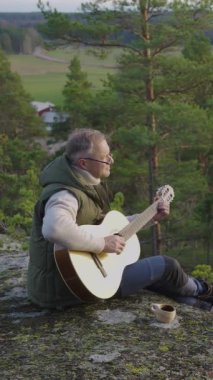 Orta yaşlı bir adam, gün batımında bir Finlandiya ormanında bir uçurumun tepesinde kuksa ahşap fincanlı kahveyle gitar çalar. Sahne, ortamın yumuşak parıltısıyla huzurlu bir çevreyi yakalıyor.