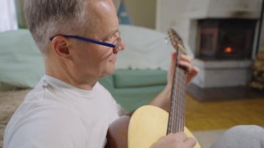 Orta yaşlı bir adam sıcak bir oturma odasında şömineli akustik gitarını tek başına çalar. Kendi solo çalışmalarına dalmış kişisel ifade ve müzikal adanmışlıktan zevk alıyor. Rahat ve...