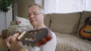Orta yaşlı bir adam rahat bir oturma odasında tek başına akustik gitarını çalar. Kendi solo çalışmalarına dalmış kişisel ifade ve müzikal adanmışlıktan zevk alıyor. Rahat ve samimi.