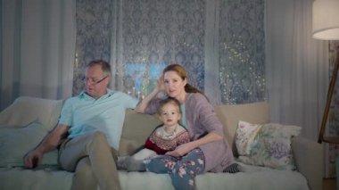 Bir aile akşam birlikte vakit geçirmekten zevk alır, rahat oturma odalarında televizyon izlerler. Ebeveynler ve çocuklar sıcak bir ışık ve rahat bir atmosferle çevrili bir kanepede rahatça oturuyorlar.