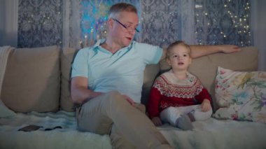 Orta yaşlı bir adam, yürümeye yeni başlamış çocuğuyla sıcak bir oturma odasında oturuyor ve akşamları televizyon seyrediyor. Oda, televizyonun parıltısıyla hafifçe aydınlatılıyor. Çocukların odaklanmış ifadesini vurguluyor..