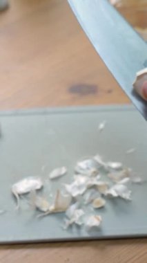 Bir kadın sarımsağı yakın çekimde bıçakla kesiyor. Salata için sarımsak kesmek ya da et için aromatik baharat olarak.