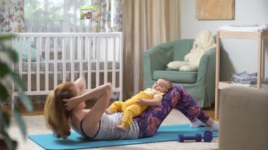 Genç, zinde bir anne, bebeği ile birlikte bebek odasında spor yapıyor. Doğum sonrasındaki genç bir anne için bir takım egzersizler. Spor, annelik, doğum sonrası ve aktif yaşam tarzı..