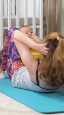 Genç, zinde bir anne, bebeği ile birlikte bebek odasında spor yapıyor. Doğum sonrasındaki genç bir anne için bir takım egzersizler. Spor, annelik, doğum sonrası ve aktif yaşam tarzı..