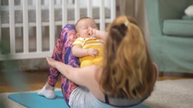 Genç, zinde bir anne, bebeği ile birlikte bebek odasında spor yapıyor. Doğum sonrasındaki genç bir anne için bir takım egzersizler. Spor, annelik, doğum sonrası ve aktif yaşam tarzı..