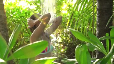 Yeşilliklerle çevrili açık havada duş alan bir kadın. Rahatlama ve doğayla bağlantı. Canlı yeşil yapraklar ve yaprakların arasından süzülen güneş ışığı. Organik cilt bakımı, lüks