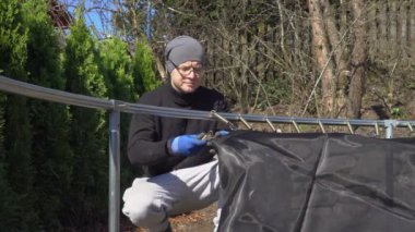 Finlandiya 'da güneşli bir bahar gününde arka bahçede trambolin monte eden bir adam. Ev geliştirme, açık hava aktiviteleri ve mevsimsel bakım