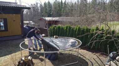 Finlandiya 'da güneşli bir bahar gününde arka bahçede trambolin monte eden bir adam. Ev geliştirme, açık hava aktiviteleri ve mevsimsel bakım