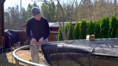 Finlandiya 'da güneşli bir bahar gününde arka bahçede trambolin monte eden bir adam. Ev geliştirme, açık hava aktiviteleri ve mevsimsel bakım