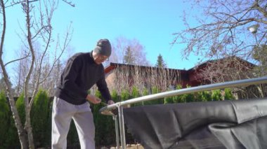 Finlandiya 'da güneşli bir bahar gününde arka bahçede trambolin monte eden bir adam. Ev geliştirme, açık hava aktiviteleri ve mevsimsel bakım