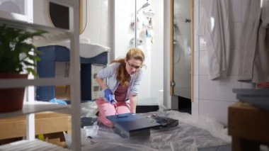 Banyoyu yenileyen bir kadın, ahşap dolabı koyu mavi renkle boyuyor. Ev geliştirme projesi, DIY yenileme, modern iç yenileme. Odaklanmış iş, aletler ve boya malzemeleri.