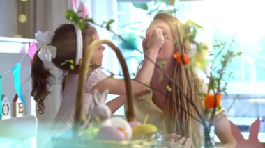 Tavşan kulaklı, annesinin yüzünü boyayan küçük bir kız. Sıcak, yaratıcı ve aile bağlarıyla dolu neşeli bir Paskalya anı. Yumuşak ışıklandırma, renkli dekorasyon, şenlikli ve mutlu atmosfer..