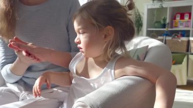 Anne, çocuğun ellerine ve ayaklarına doğal ışık altında nemlendirici krem sürüyor. Nazik cilt bakımı, ebeveyn-çocuk bağı ve sağlıklı cilt koruması. Yakın çekim, sıcak atmosfer, kişisel bakım.
