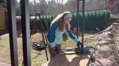 Kararlı bir kadın elektrikli testere bıçağını keskinleştirir, bahçe işi için hazırlanır. Kendi kendine yetebilme ve yetkinliği benimsiyor. Açık hava bakımının herkes için olduğunu kanıtlıyor. Bahar yenilenmesi devrede.