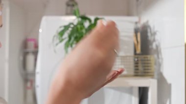 Beyaz bornozlu bir kadın aynaya bakarken anti-reşit bir yüz serumu kullanıyor. Yumuşak doğal ışık, cilt bakımı, güzellik ve kendine özen..