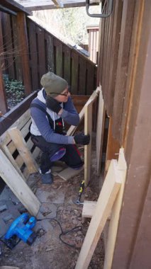 Eski ahır tadilatı sırasında dışarıda ahşap duvar onarımı yapan adam. Yapıyı geliştirmek için el aletleri ve kereste kullanıyor. DIY, İnşaat ve Ev Bakımı.