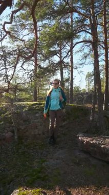 Sırt çantalı genç bir kadın sık yeşil ormanda yosun kaplı kayalık bir uçurumda yürüyüş yapıyor. Gün ışığı ağaçların arasından parlıyor, huzurlu ve maceracı atmosfer, farkındalık, doğayla bağlantı.