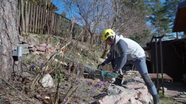 Evin yakınındaki bir ağaç kütüğünü kesmek için elektrikli testere kullanan yetişkin bir adam. DIY, bahçıvanlık, peyzaj ve mevsimlik bakım kavramı.