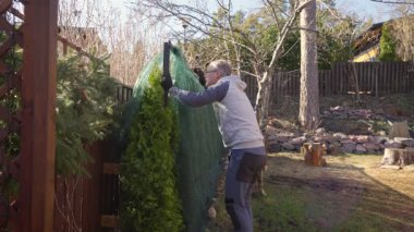 Baharda arka bahçedeki çitlerden koruyucu ağları söken adam.