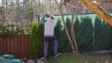 Baharda arka bahçedeki çitlerden koruyucu ağları söken adam.