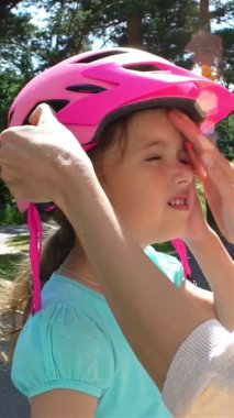 Annem güneşli bir günde kızların kafalarına parlak pembe bir bisiklet kaskı takar. Orman parkında at sürmeden önce güvenliği sağlar..