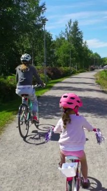 Finlandiya 'da yeşil bir parkta güneşli bir günde kask takan anne ve kız bisiklet sürerler. Aile zamanı, açık hava aktivitesi ve doğada sağlıklı yaşam tarzı..