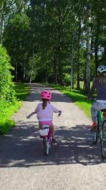 Finlandiya 'da yeşil bir parkta güneşli bir günde kask takan anne ve kız bisiklet sürerler. Aile zamanı, açık hava aktivitesi ve doğada sağlıklı yaşam tarzı..