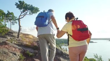 Finlandiya 'da deniz kenarındaki kayalık bir tepede el ele yürüyüş yapan üst düzey bir çift. Yaşlı adam ve kadın sırt çantası takıyor, açık hava macerasının, desteğin ve yaşlılığın tadını çıkarıyorlar..