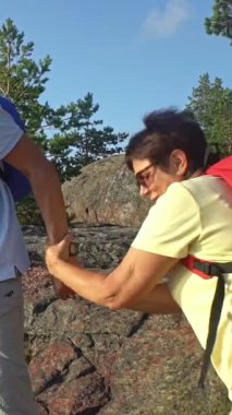 Finlandiya 'da deniz kenarındaki kayalık bir tepede el ele yürüyüş yapan üst düzey bir çift. Yaşlı adam ve kadın sırt çantası takıyor, açık hava macerasının, desteğin ve yaşlılığın tadını çıkarıyorlar..