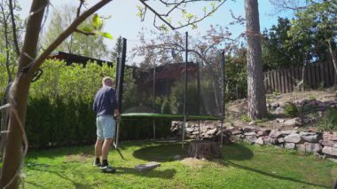 Güneşli bahar gününde aile trambolin topluyor. Baba ve kızı birlikte çerçeve kuruyorlar. Açık hava aktivitesi, takım çalışması, ev bahçesi sahnesi..