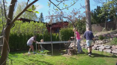 Güneşli bahar gününde arka bahçede trambolin toplayan iki çocuklu bir aile. Açık hava aktivitesi, takım çalışması, ev bahçesi sahnesi..