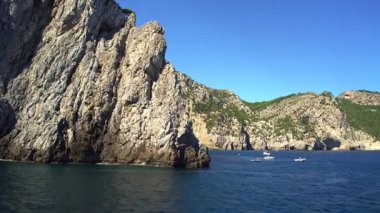 Uçsuz bucaksız uçurumları, derin mavi denizi ve açık bir yaz gününde sudaki tekneleri olan Mallorca 'nın kayalık kıyı şeridi panoramik manzarası. İzleme görüntüsü