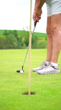 Yuvarlanan tepelerle manzaralı bir sahada golf oynayan aktif son sınıf öğrencisi bir kadın güneşli bir yaz gününde açık hava egzersizinin ve hareketli bir emekliliğin tadını çıkarıyor..