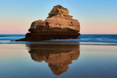 Kireçtaşı kayaları alçak gelgitte yansır. Pürüzsüz suyla uzun pozlu çekim. Portekiz, Portimao 'da Praia dos Tres Castelos