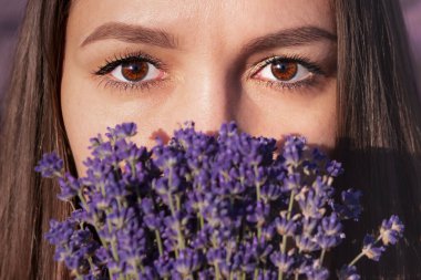 Bir kadının yüzünün yakın plan görüntüsü. Ön planda lavanta buketi