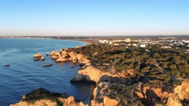 Gündoğumunda Algarve sahilinin altın tepelerinin üzerinden insansız hava aracı uçuşu. Portimao, Portekiz