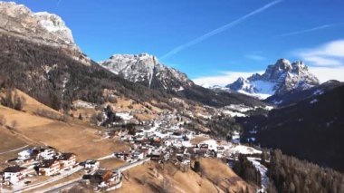 Kışın güneşli bir günde Dolomite Alpleri 'ndeki küçük bir İtalyan köyünün üzerinde uçmak. 4K İHA görüntüleri