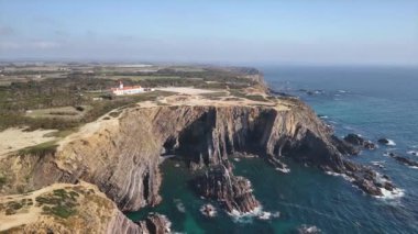 Portekiz 'in batısındaki Farol do Cabo Sardao fenerine doğru uçuyor. Yüksek kayalıklar ve gök mavisi okyanus altında