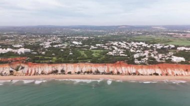 İnsansız hava aracı Praia da Falesia 'ya doğru uçuyor, Portekiz' in güneyine. Tepelerdeki kırmızı renkli kayalıkların, golf kortlarının ve çam ağaçlarının manzarası