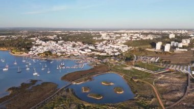 Alvor köyünün en üst manzarası, tekneli limanı, kum tepeleri, tahta tahta kaldırımlı bataklıkları, ve günbatımında Praia da Torralta. Algarve bölgesi, Portekiz