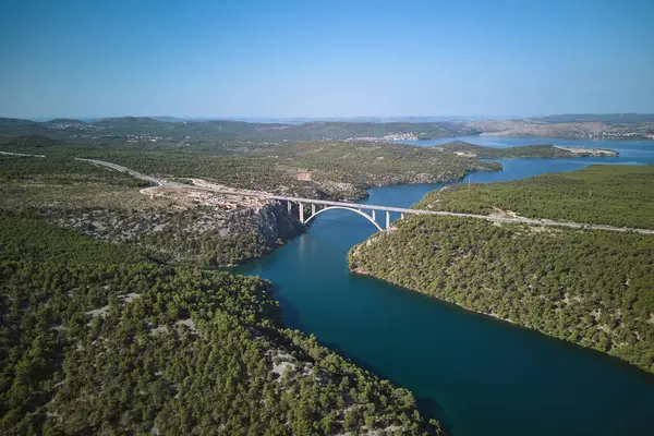 Hırvatistan 'ın Krka Ulusal Parkı' ndaki karayolu ve nehir üzerindeki kemer köprüsünün panoramik manzarası. Prokljan Gölü arka planda.